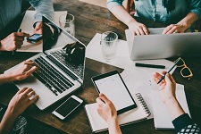 Several people collaborating together at a table, using laptops, notepads, and other tools.